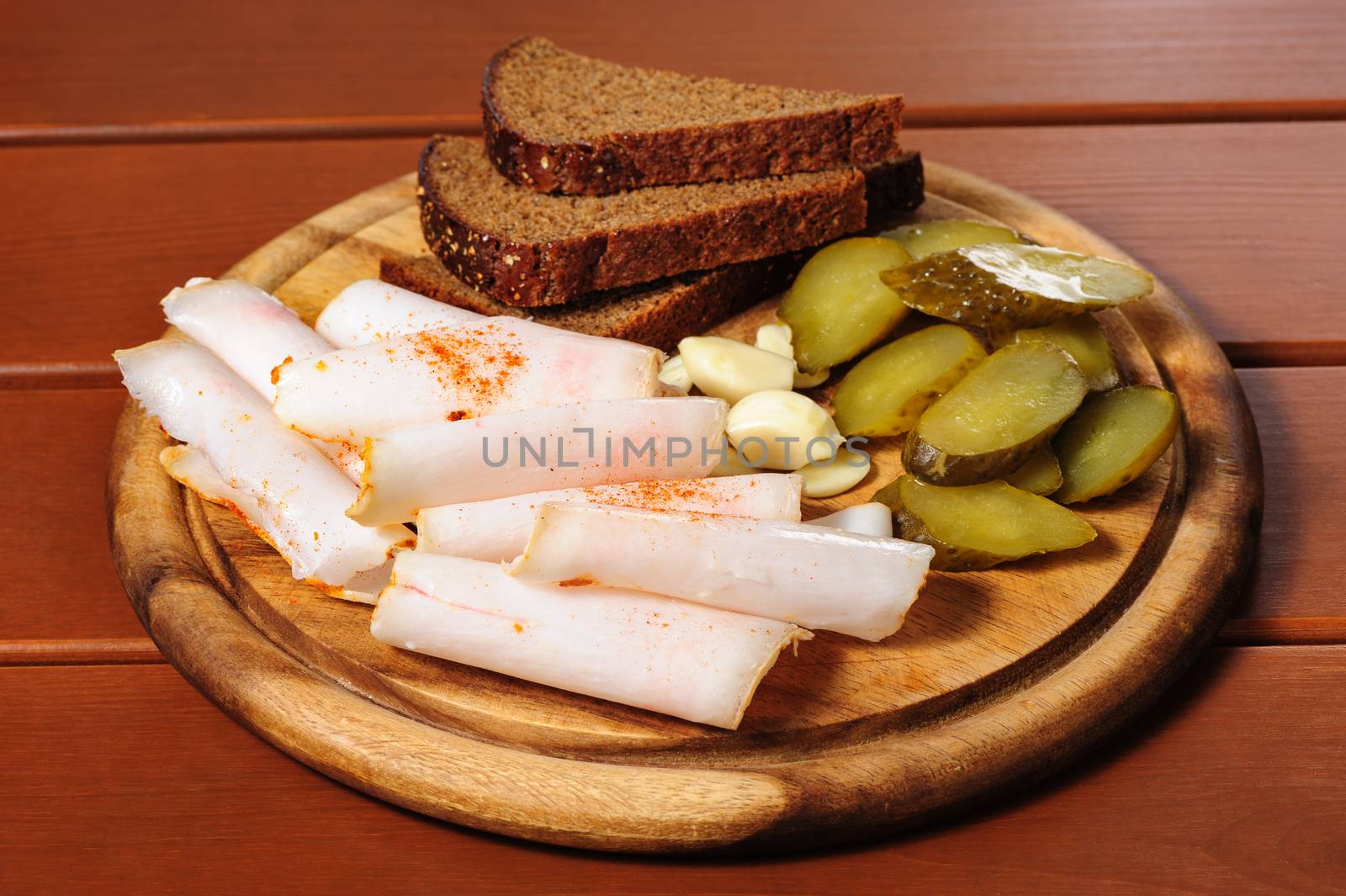 Big wooden plate with slices of smoked bacon, pickled cucumbers and rye bread, Russian traditional snacks for vodka, beer and other alcohol bewerages
