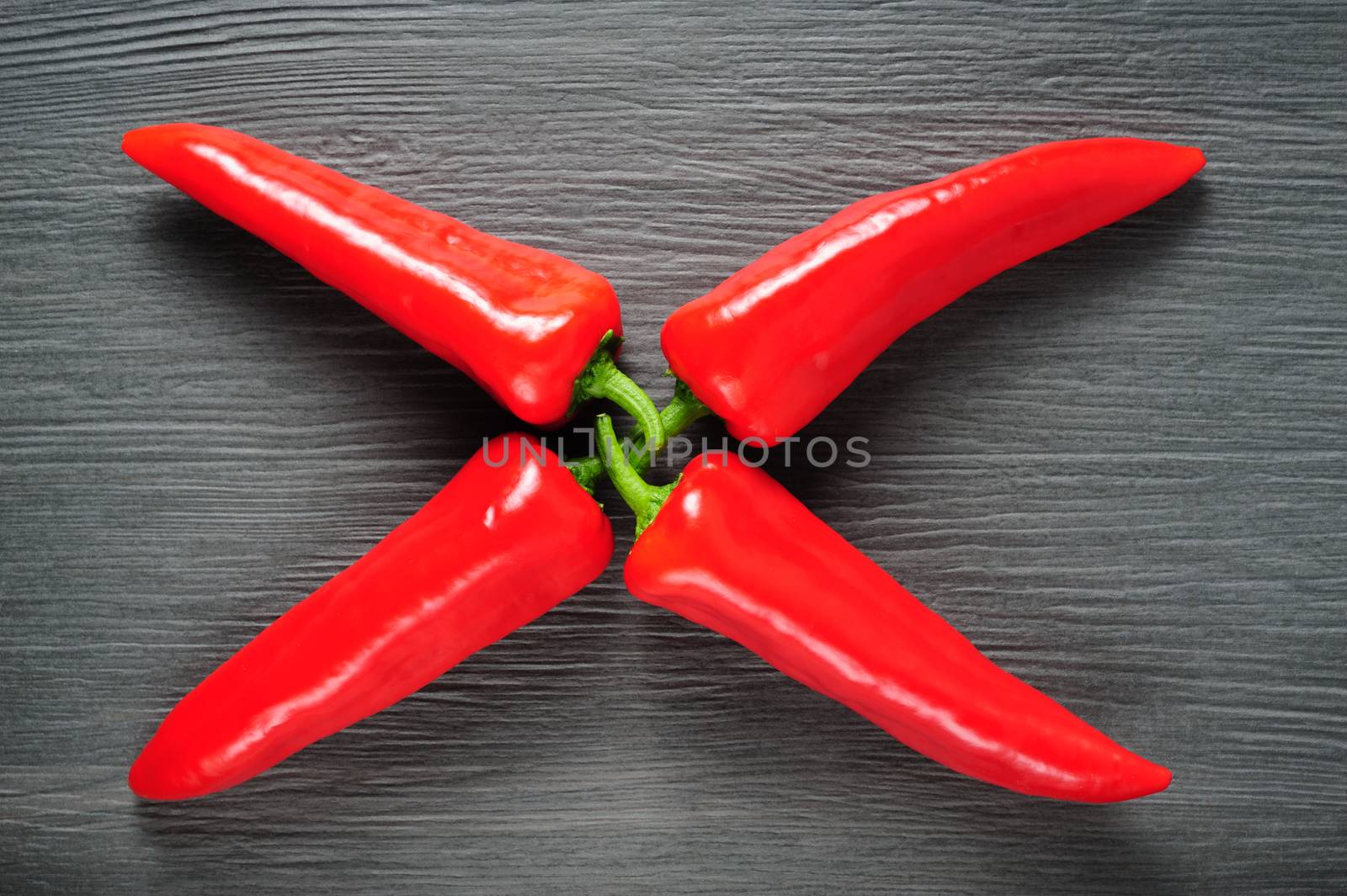 X shaped figure made of four ripe sweet red Kapia peppers on dark shale stone background