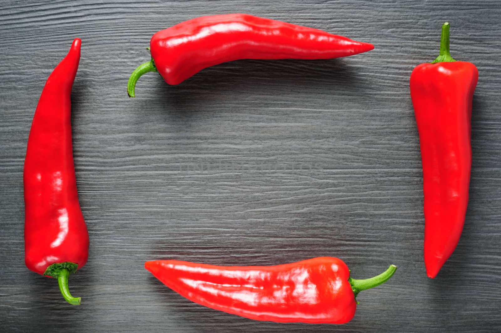 Frame made of four ripe sweet red Kapia peppers on dark shale stone background