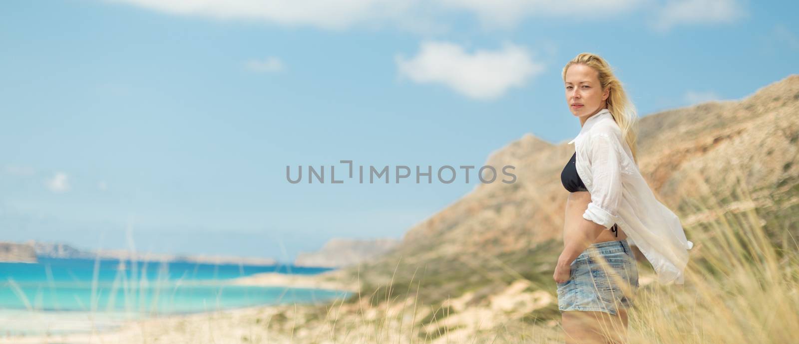 Relaxed woman in white shirt looking at distance, enjoying beautiful nature, freedom and life at serene landscape at Balos beach, Greece. Concept of vacations, freedom, happiness, joy and well being.