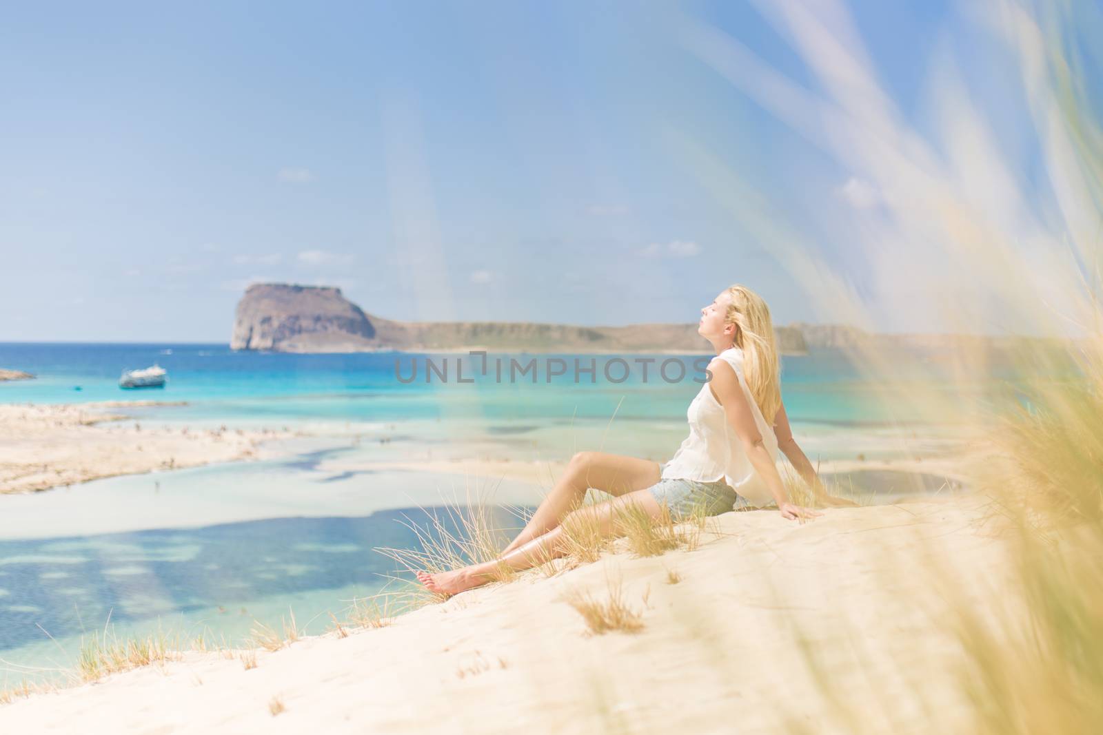 Relaxed woman enjoying sun, freedom and life an a beautiful sandy beach of Balos in Greece. Young lady feeling free, relaxed and happy. Vacations, freedom, happiness, enjoyment and well being.