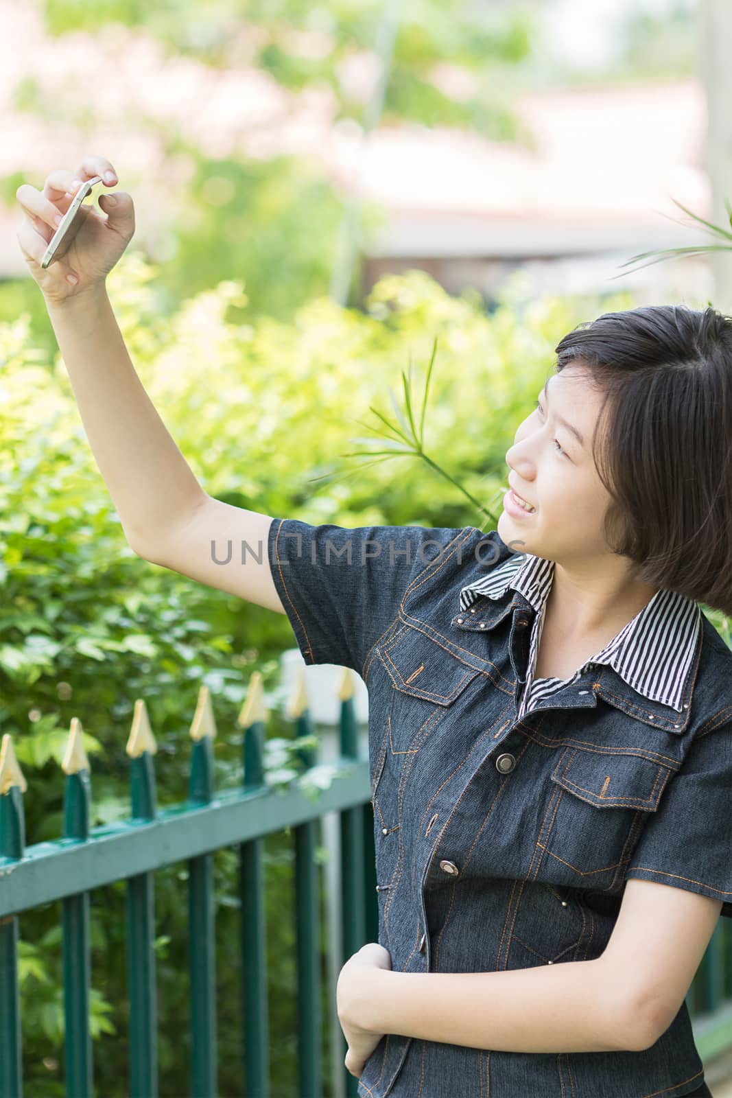 Asian girl with short hair using mobile phone to take selfie outdoor in garden