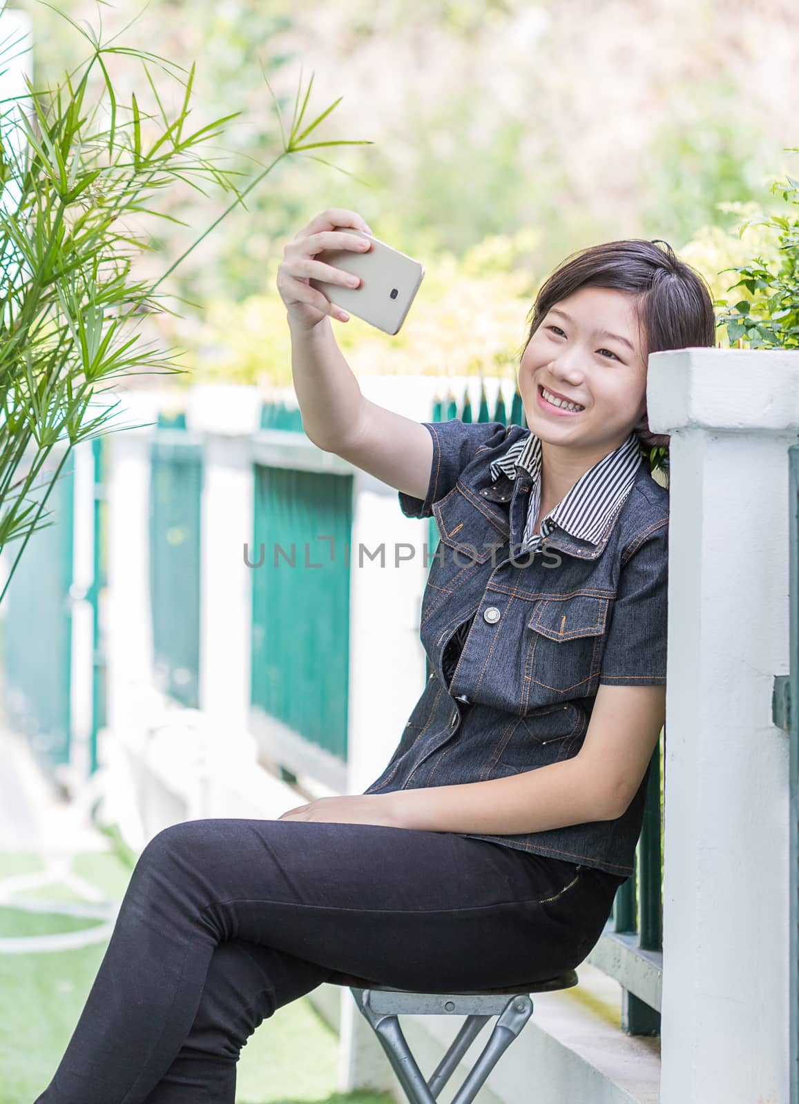 Asian girl with short hair using mobile phone to take selfie outdoor in garden