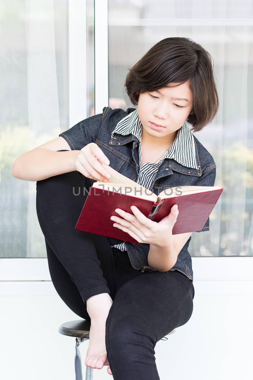 Asian girl with short hair reading a book sitting on a chair