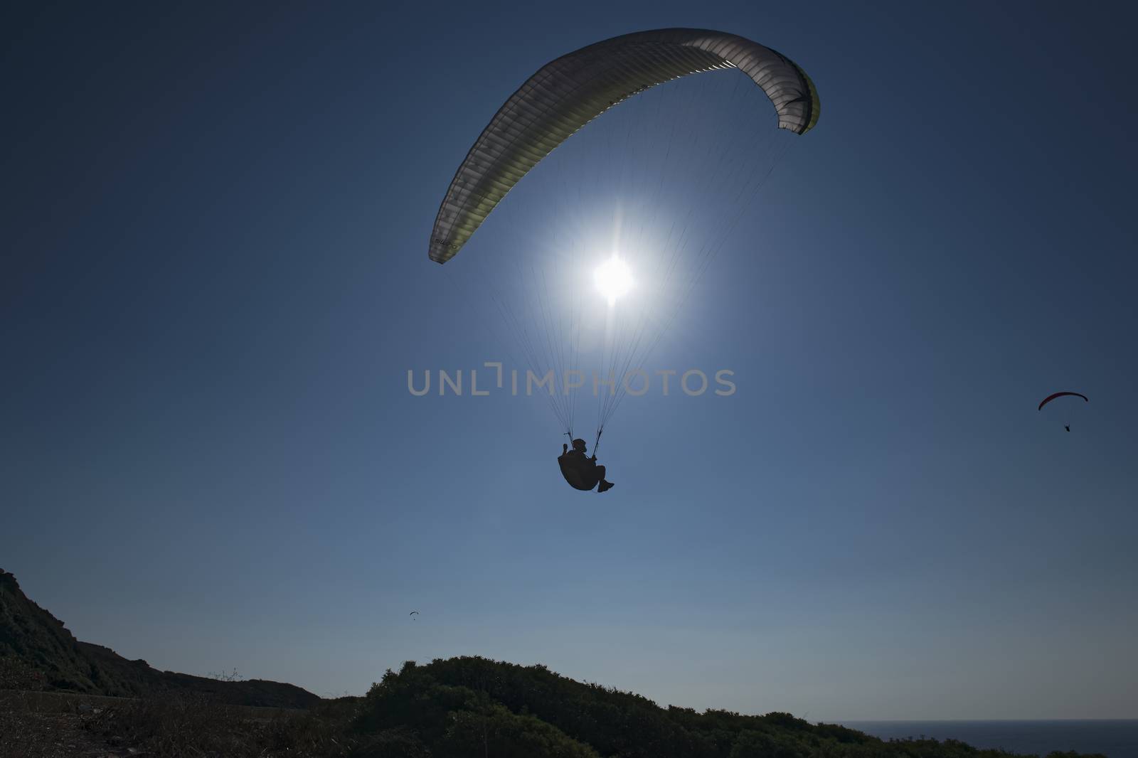 Sport paragliding in backlight with blue sky background and sun in front. Silohuette.