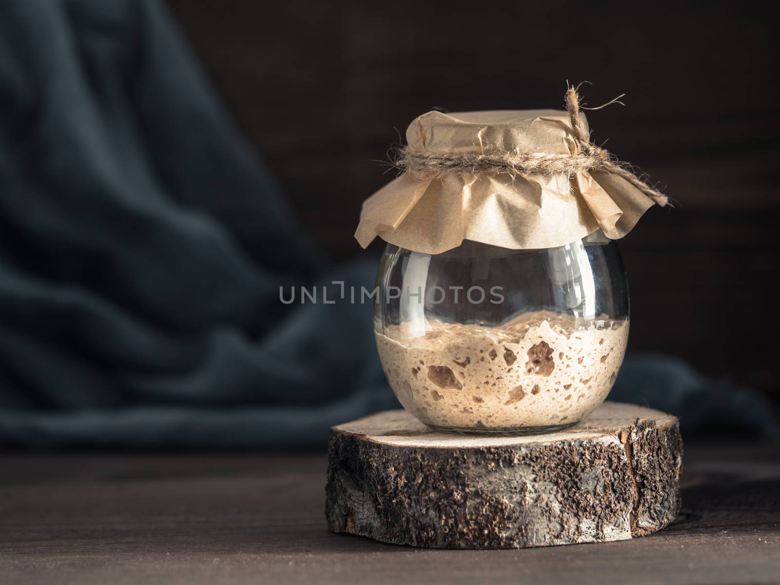 Active rye sourdough starter in glass jar on brown wooden background. Starter for sourdough bread. Toned image. Copy space.