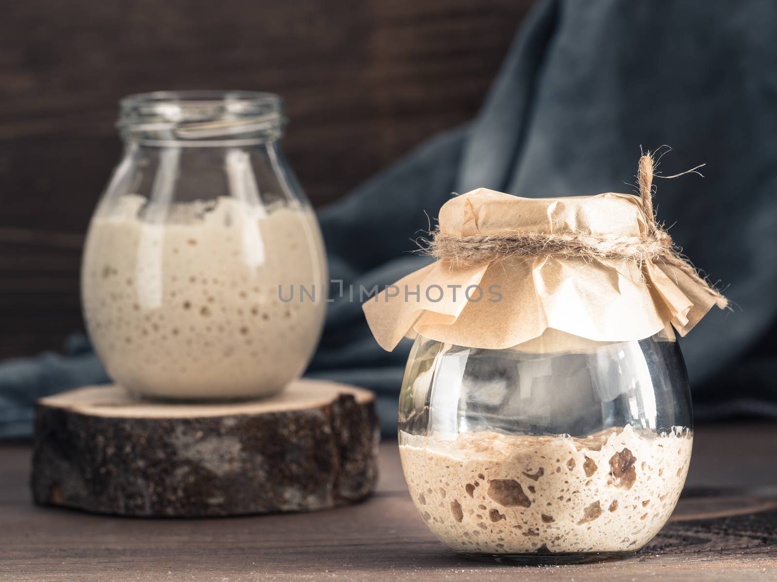 Active rye and wheat sourdough starter in glass jar on brown wooden background. Starter for sourdough bread. Toned image. Copy space.