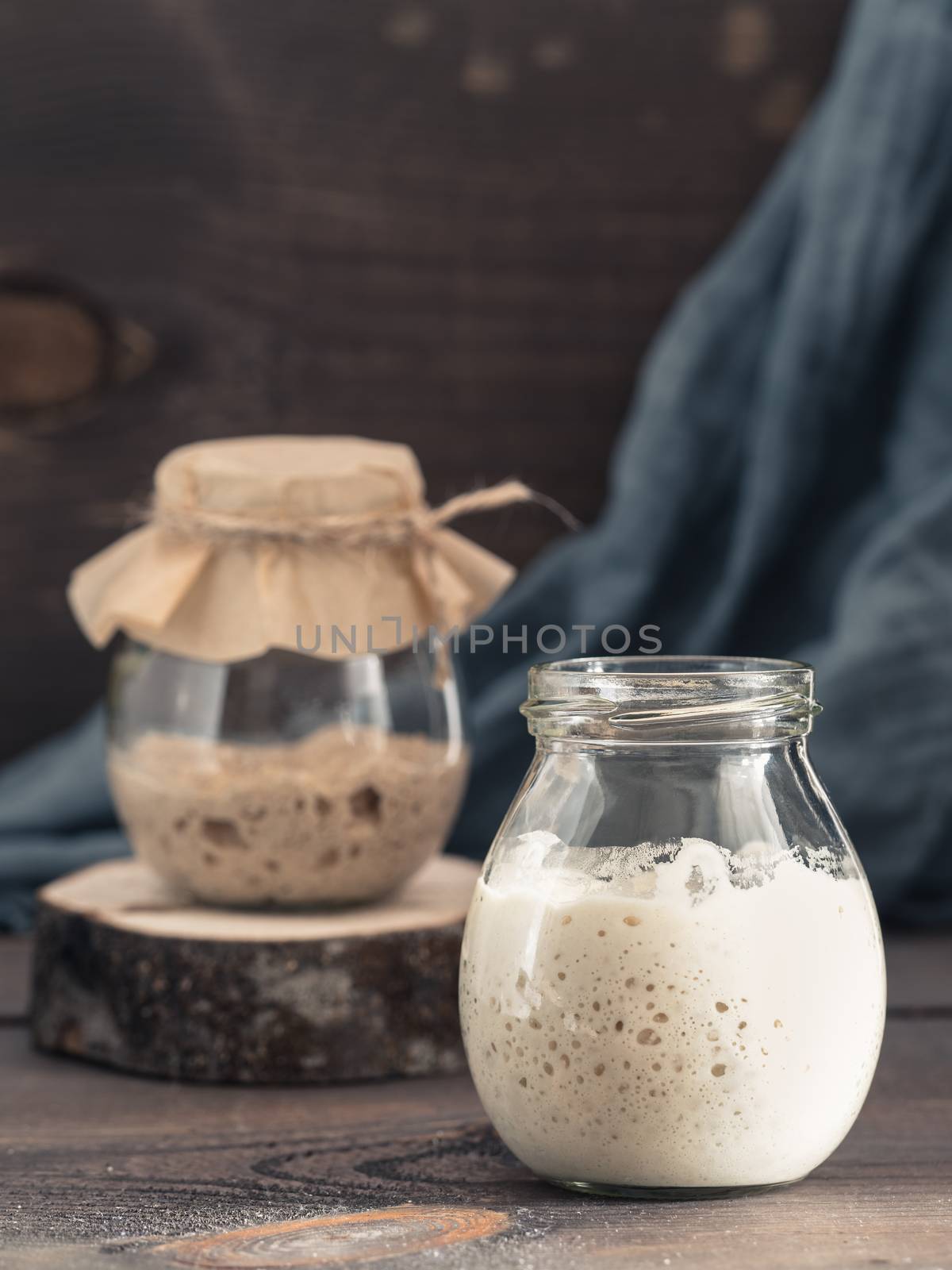 Active wheat and rye sourdough starter in glass jar on brown wooden background. Starter for sourdough bread. Toned image. Copy space. Vertical