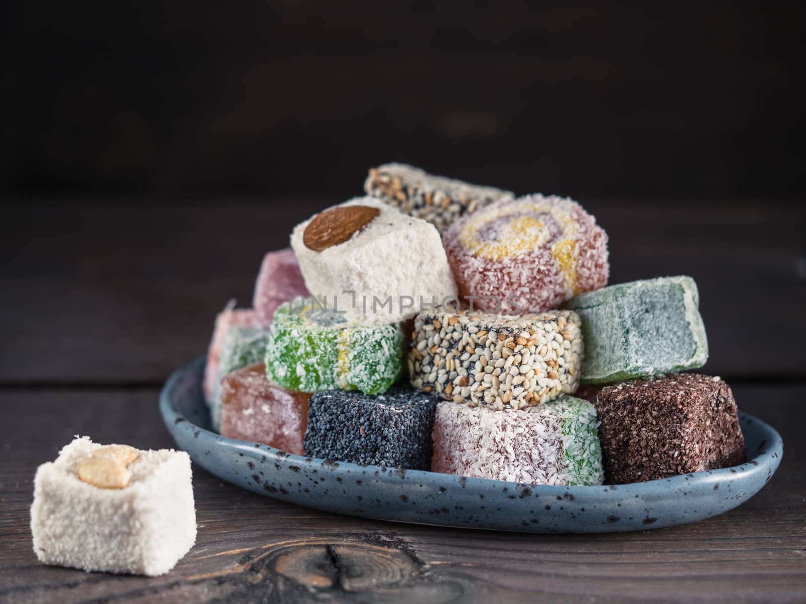 Closeup view of assortment turkish delight in blue trandy plate on dark wooden background. Copy space. Low key