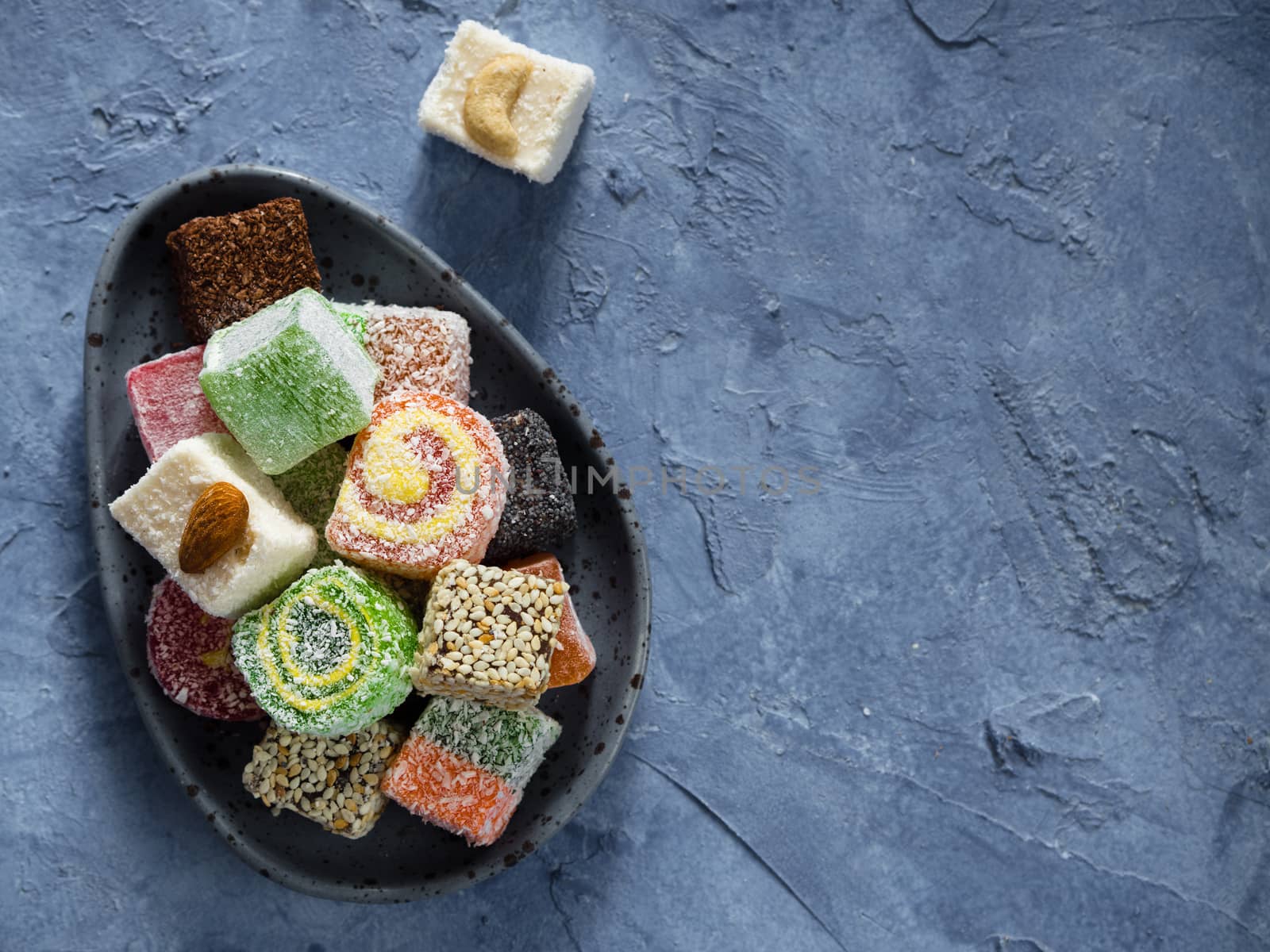 Turkish delight on blue concrete background. Assortment of traditional easten sweet dessert in trandy blue plate. Selective focus. Top view or flat lay. Copy space.