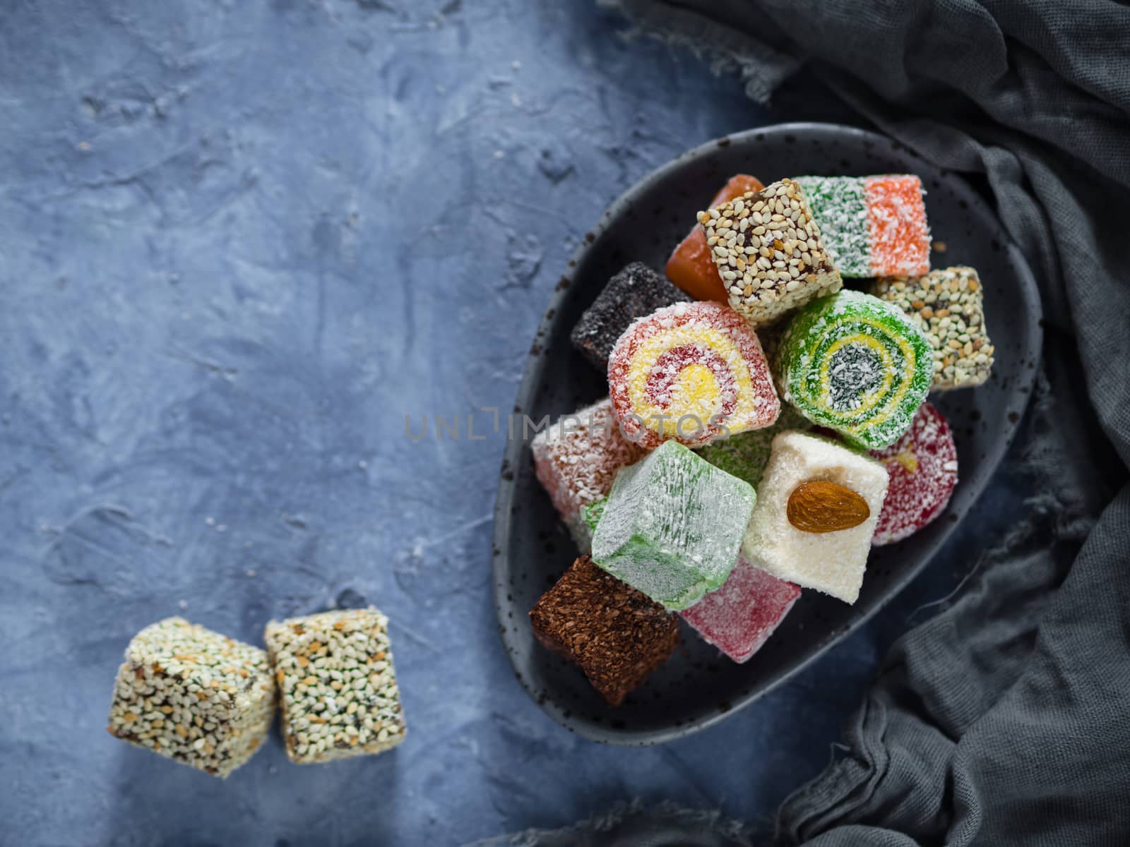 Turkish delight on blue concrete background. Assortment of traditional easten sweet dessert in trandy blue plate. Selective focus. Top view or flat lay. Copy space.