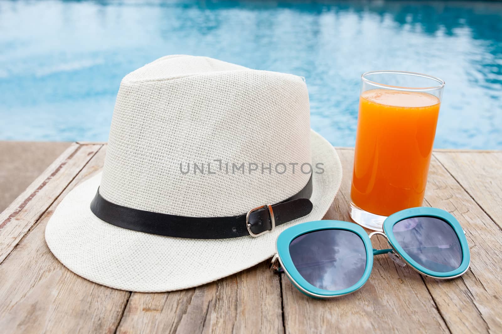 Summertime orange juice hat and sunglasses relax near swimming pool.