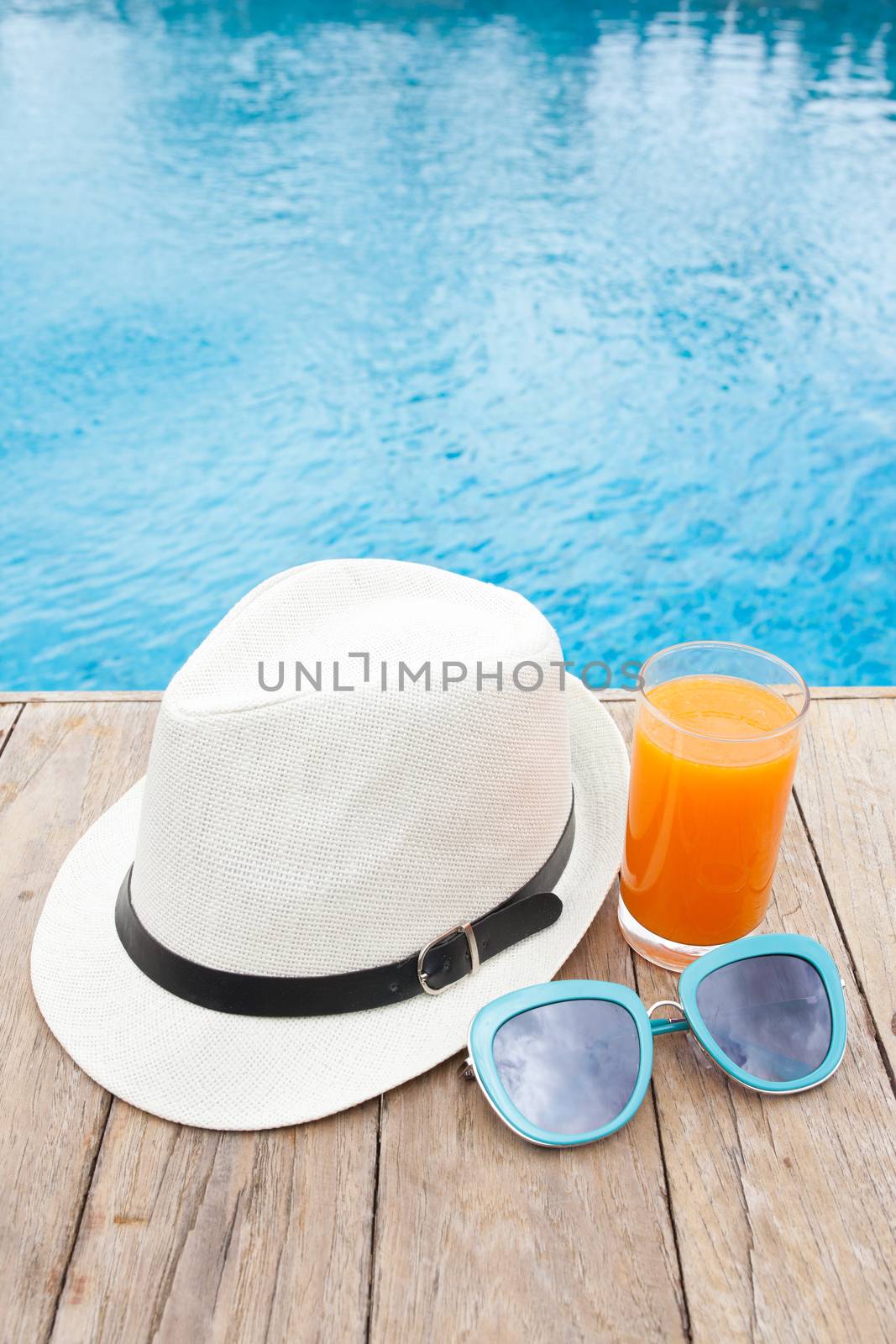 Summertime orange juice hat and sunglasses relax near swimming pool.