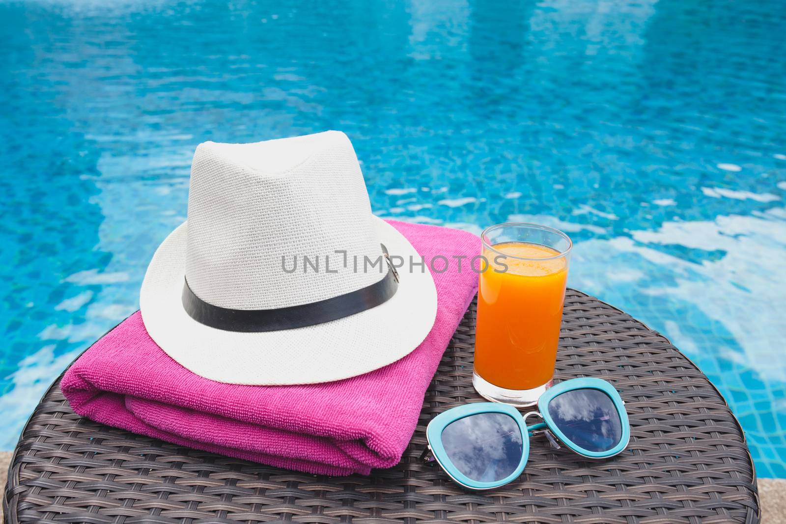 Summertime orange juice hat and sunglasses relax near swimming pool.