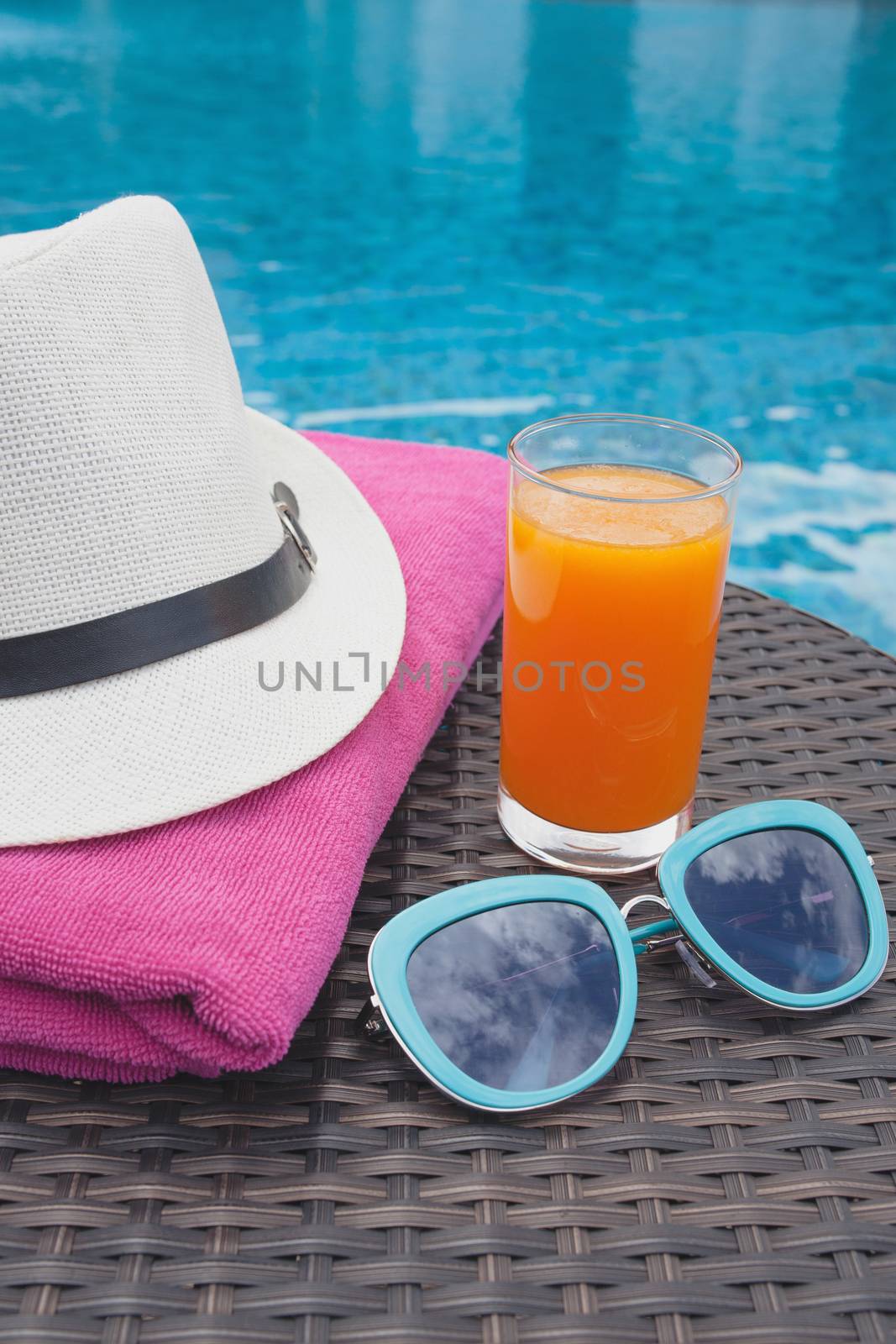 Summertime orange juice hat and sunglasses relax near swimming pool.