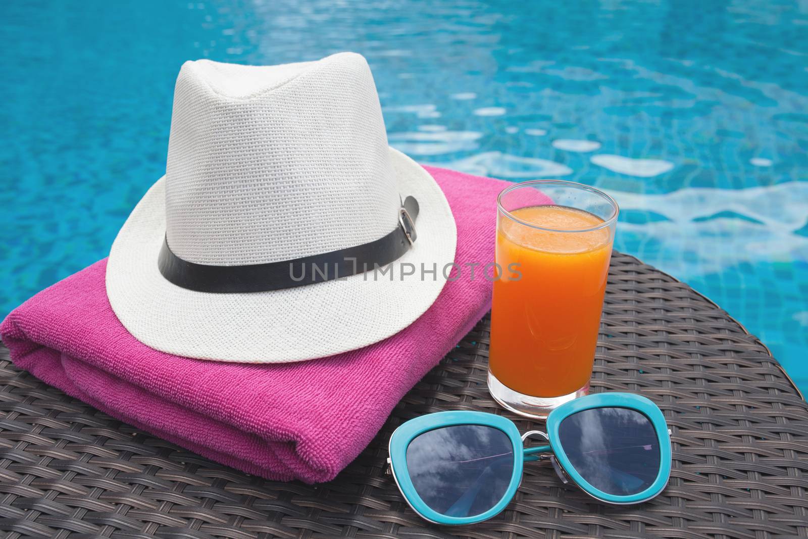 Summertime orange juice hat and sunglasses relax near swimming pool.