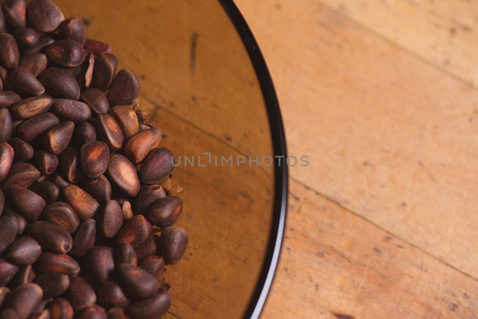 Pine nuts in shells of ciberian cedar as a background in glass bowl on wooden floor. Copyspace by skrotov