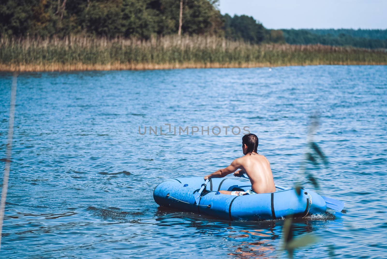 Man fisherman rows from rubber boat on a beautiful day in lake at dusk. Wide shot. Back View by skrotov