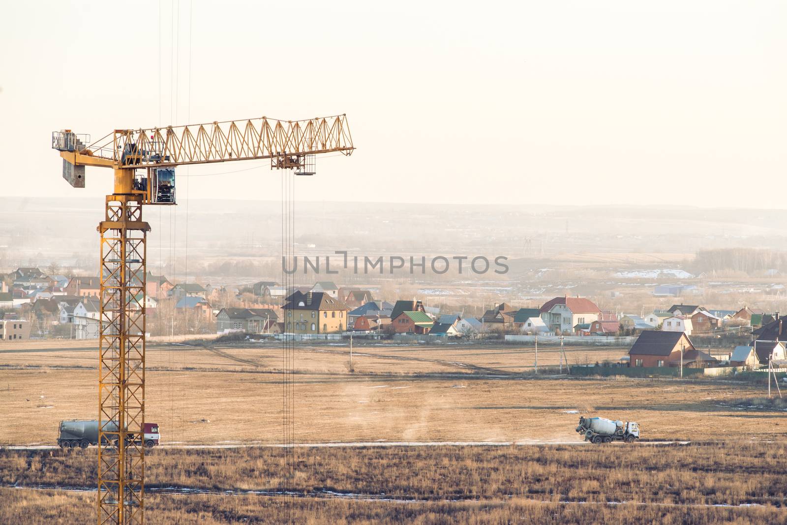 House under construction with a tower crane and two trucks on background.