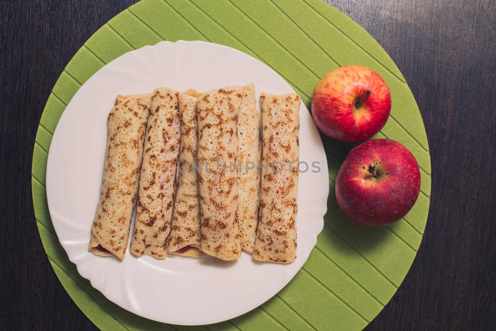 Roasted rolled pancakes on a white round plate and two apples near. Top view . Flat lay by skrotov