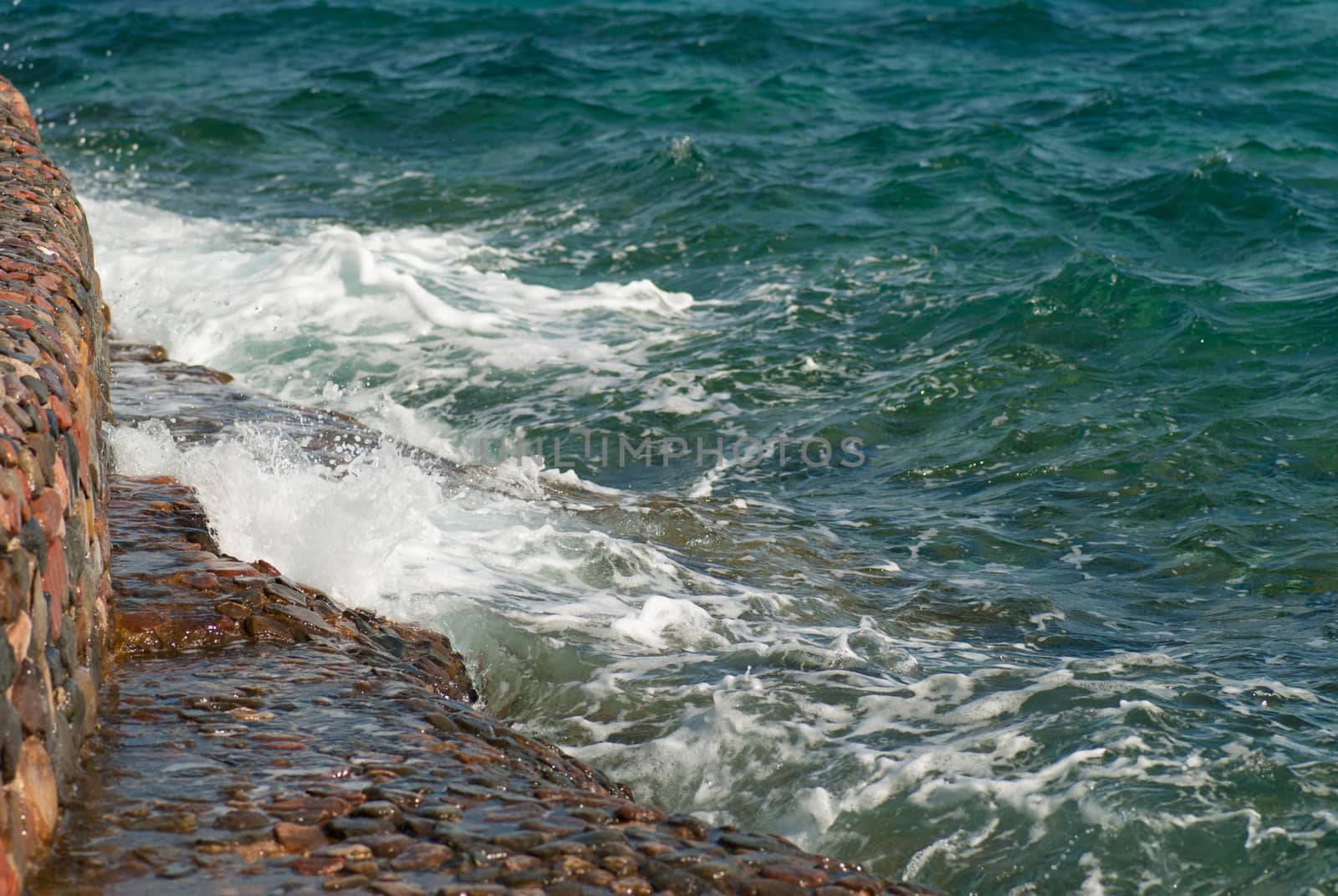 Photo of beautiful clear turquoise sea ocean water surface with ripples and bright splash on stone seascape background, horizontal picture.