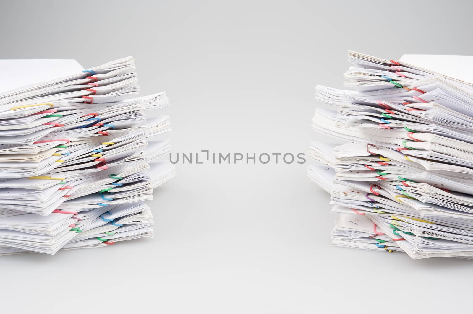 Dual pile overload of document with colorful paper clip place on white table.