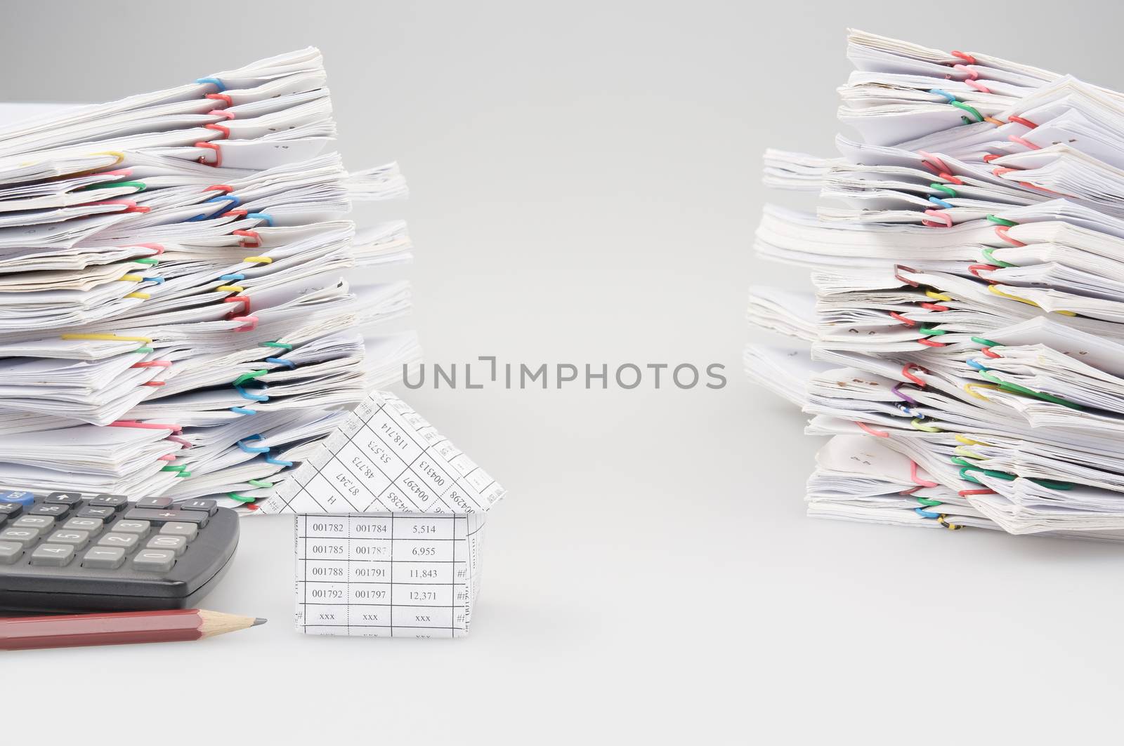 House with pencil and calculator with dual pile overload document of report and receipt with colorful paperclip on white background.