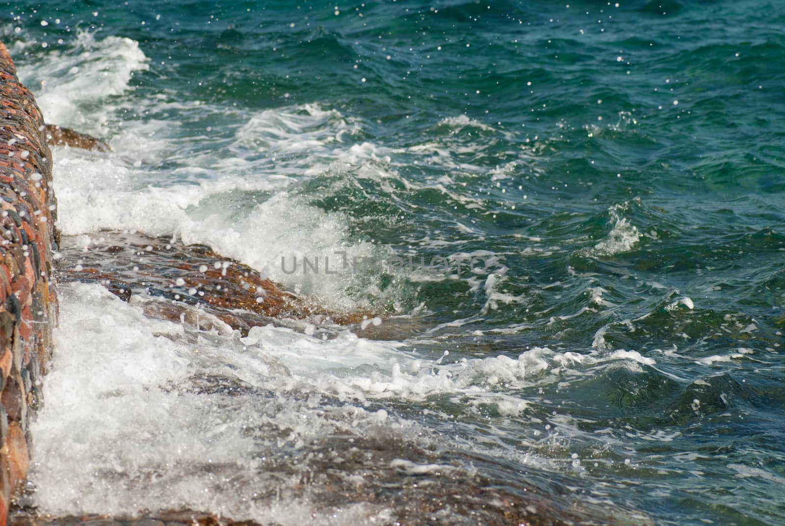 Photo of beautiful clear turquoise sea ocean water surface with ripples and bright splash on stone seascape background, horizontal picture.