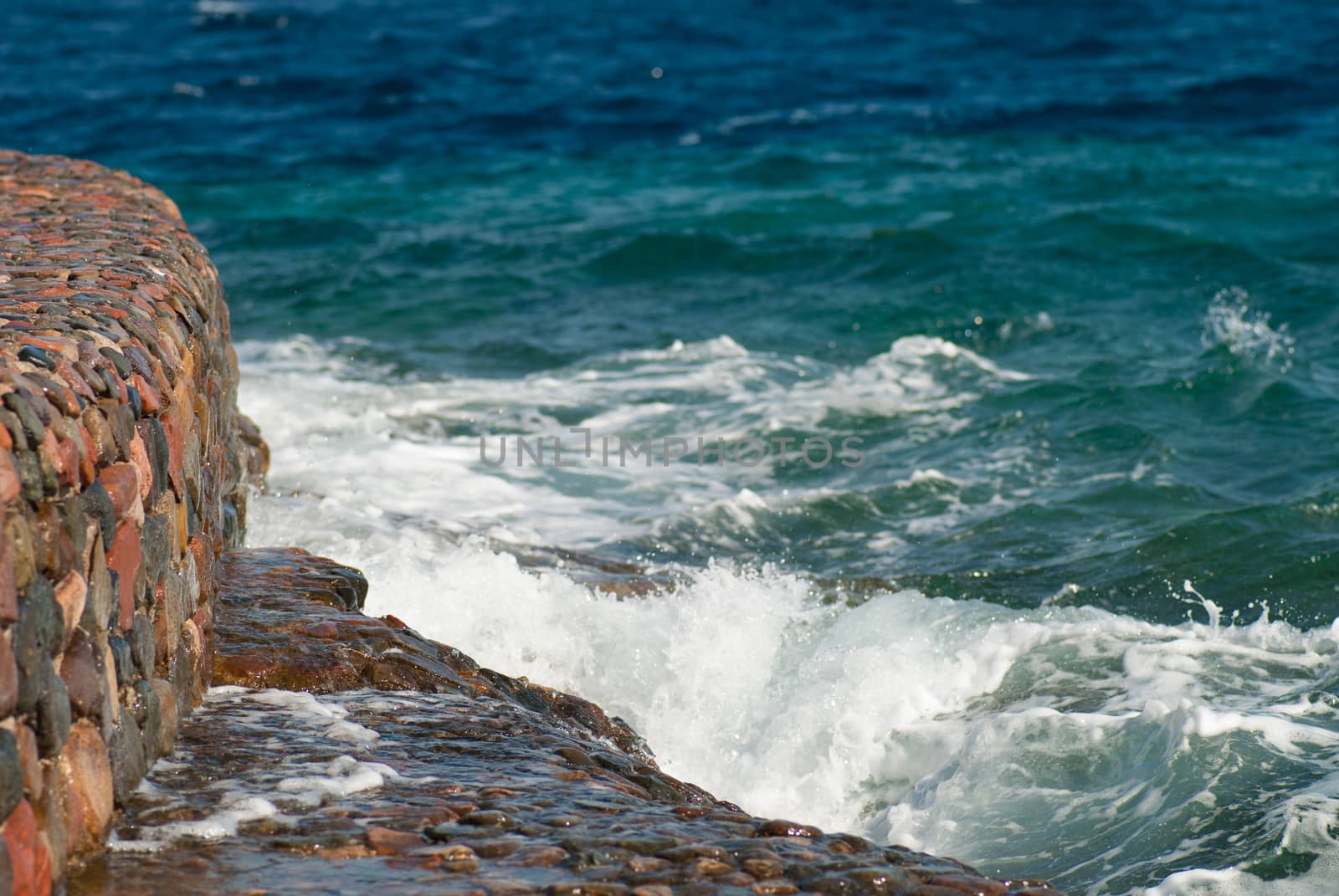 Photo of beautiful clear turquoise sea ocean water surface with ripples and bright splash on stone seascape background, horizontal picture.