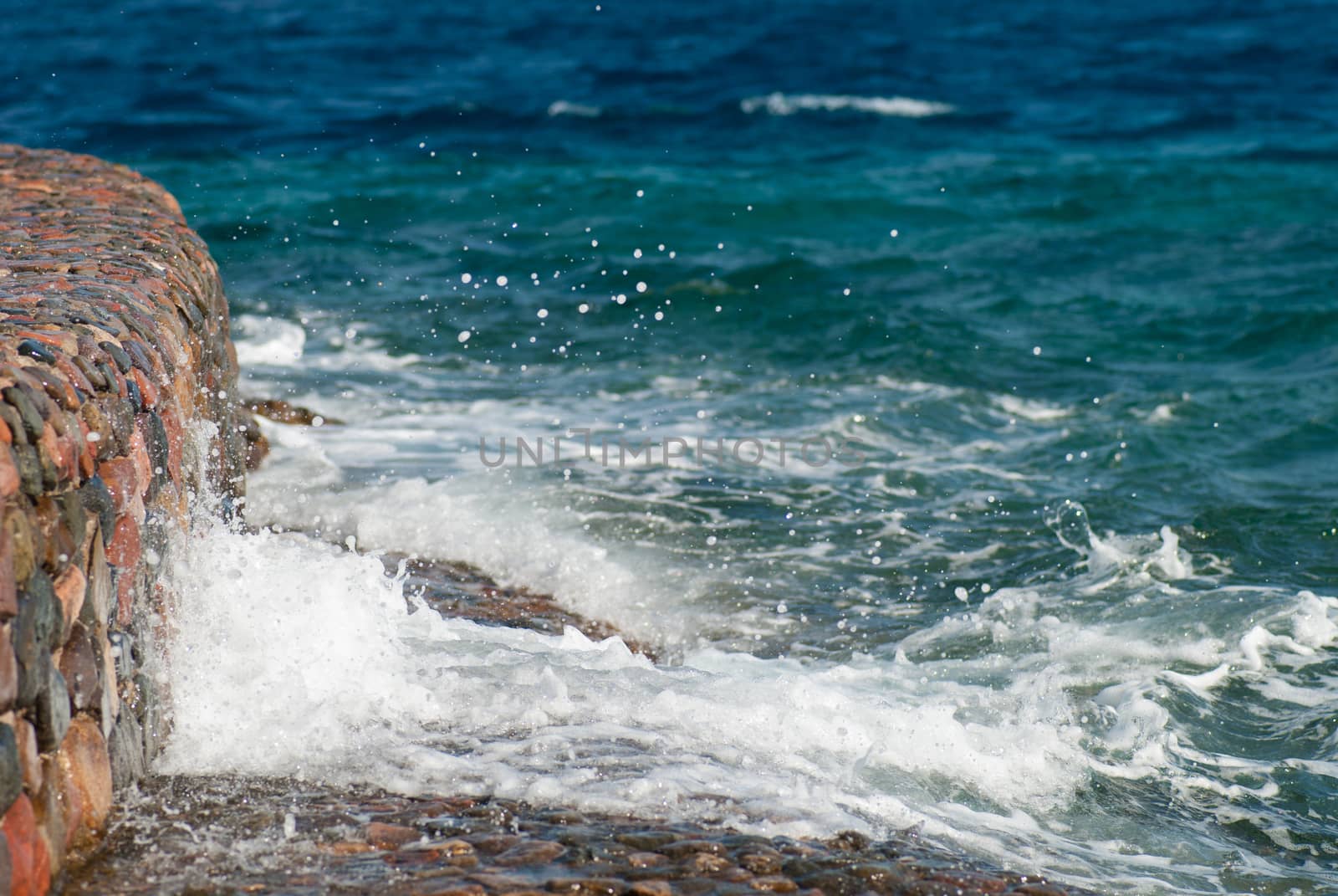 Photo of beautiful clear turquoise sea ocean water surface with ripples and bright splash on stone seascape background, horizontal picture.