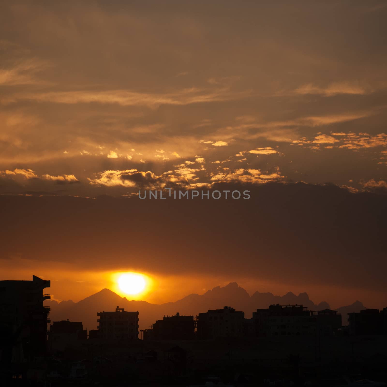 Sunset at city of Hurghada with buildings and mountains silhouette.