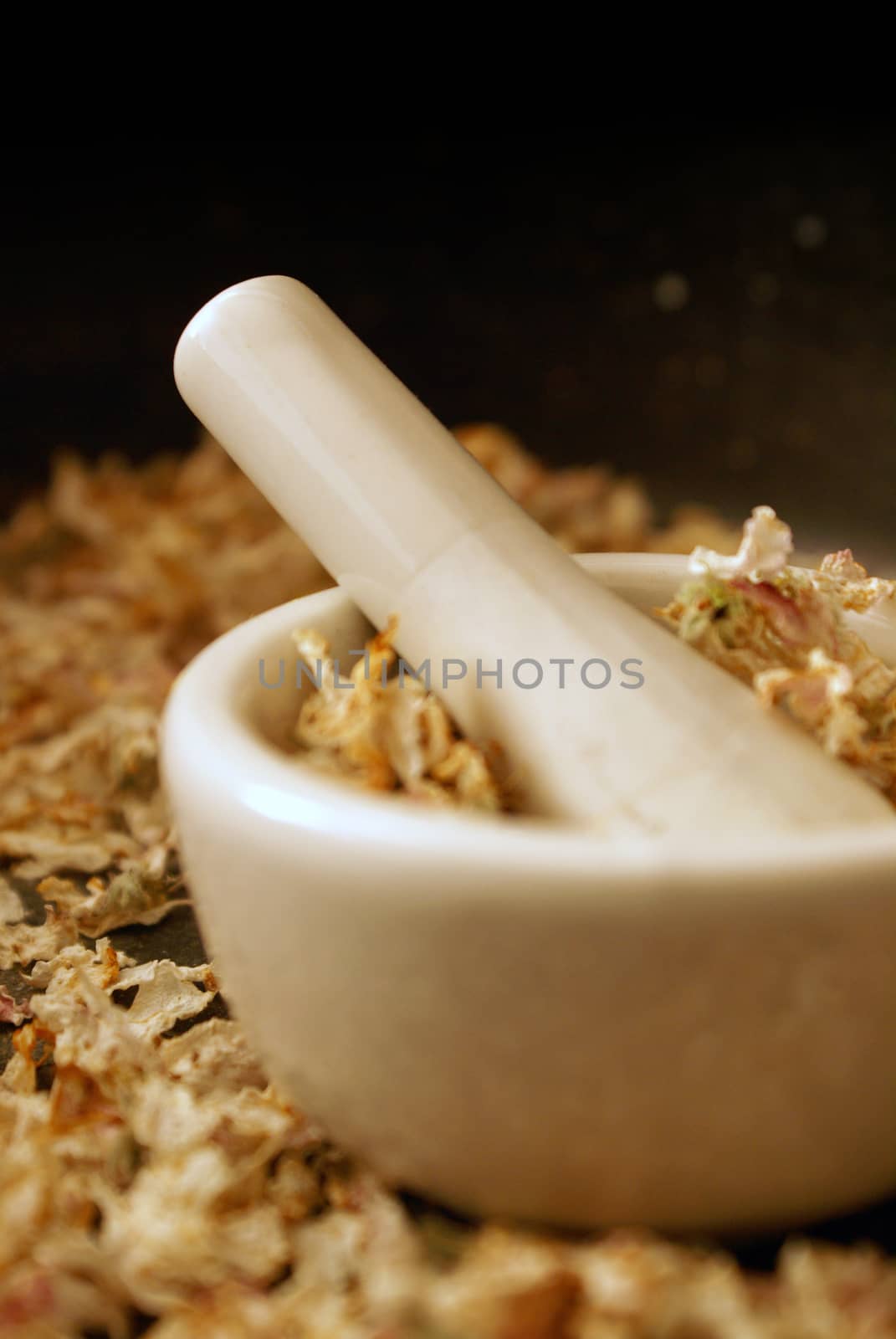 A vertical orientation of a mortar and pestle ready for preparing some dried Apple Blossoms into herbals for medical uses.