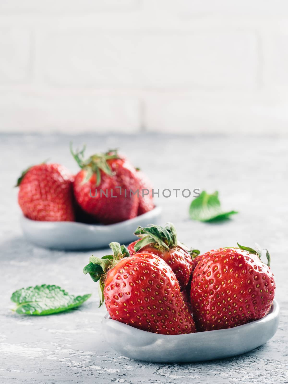 Fresh ripe strawberries in small trendy plate. Strawberry in gray plate and mint leaves on gray concrete background Copy space. Vertical.