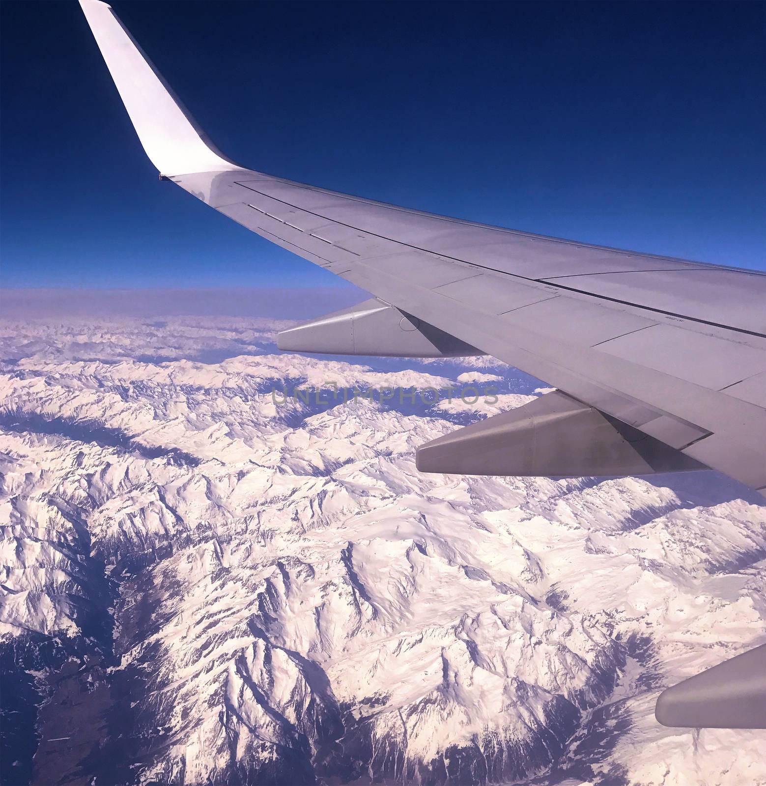 Window view from the cabin of a plane while flying over the Alps Mountain Range.