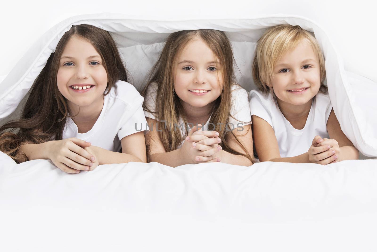 Three happy smiling children under one blanket in bed