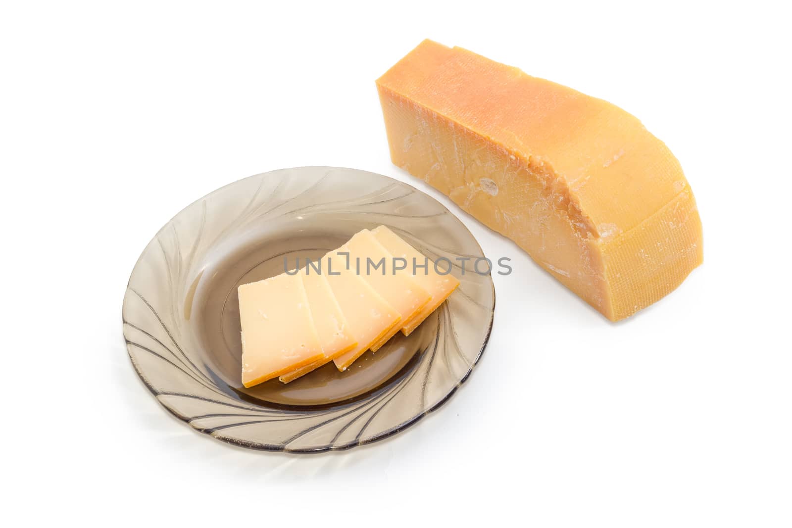 Several thin slices of the Dutch hard cheese Beemster on a dark glass saucer and piece of the same cheese beside on a light background
