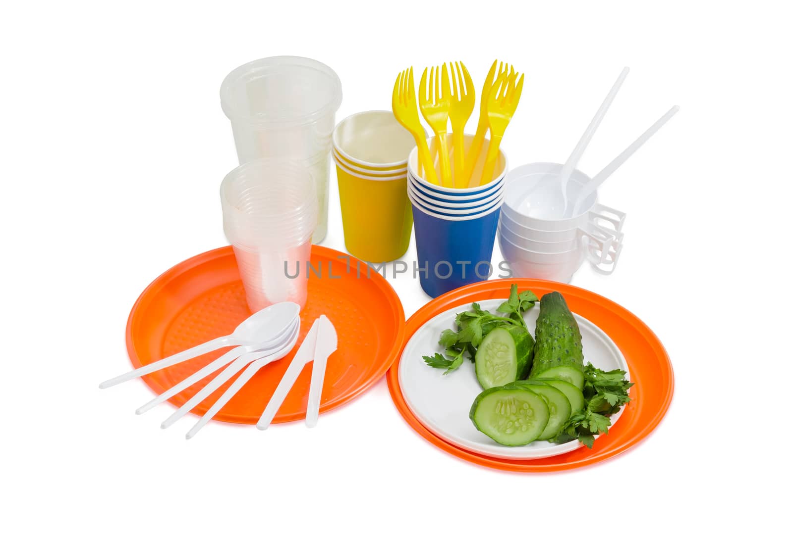 Orange and white disposable plastic plate with whole and sliced cucumber, disposable forks, spoons and knifes, paper and different plastic disposable cups beside on a light background
