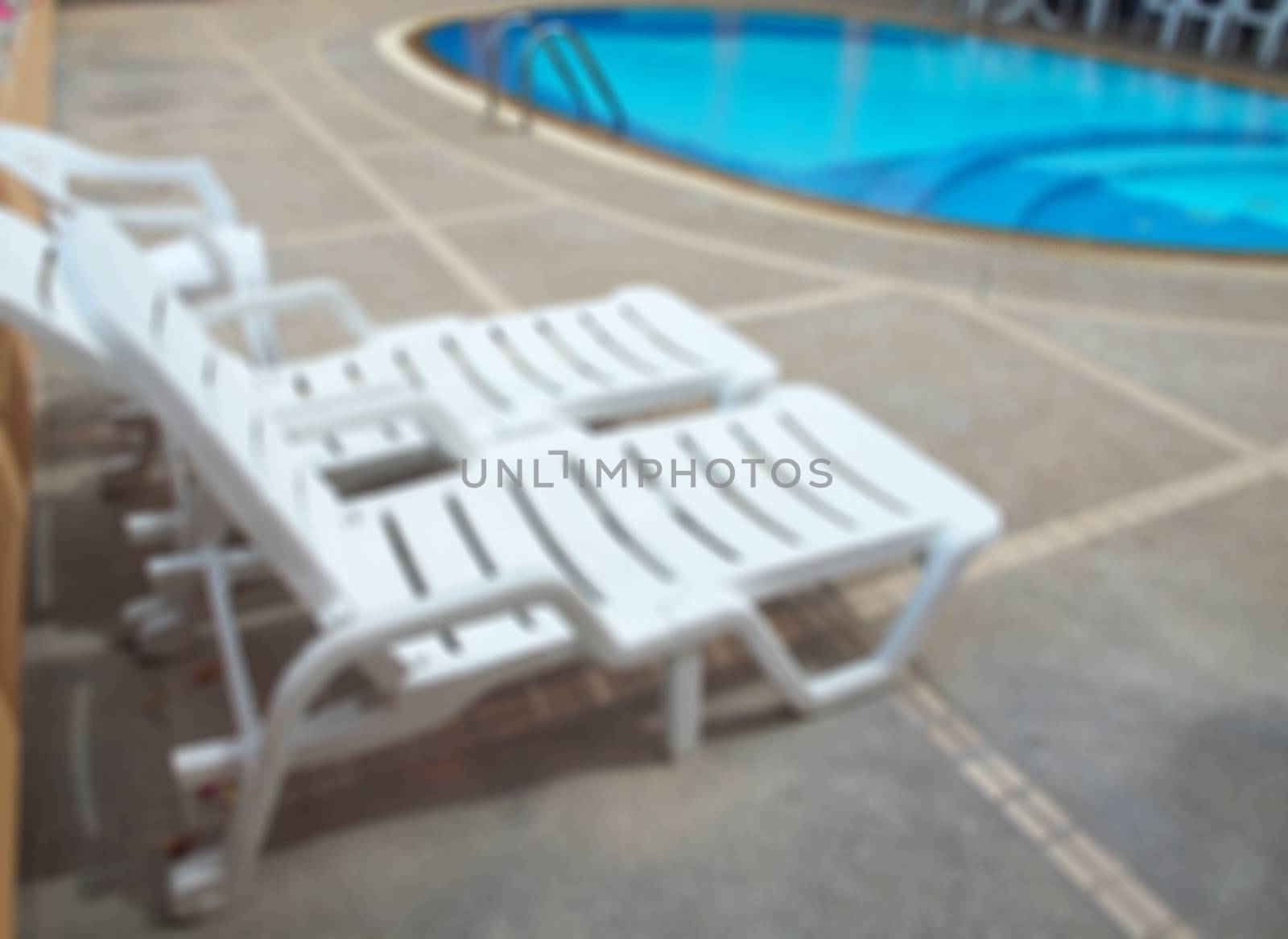 Abstract blurred swimming pool with chaise loungue on terrace.