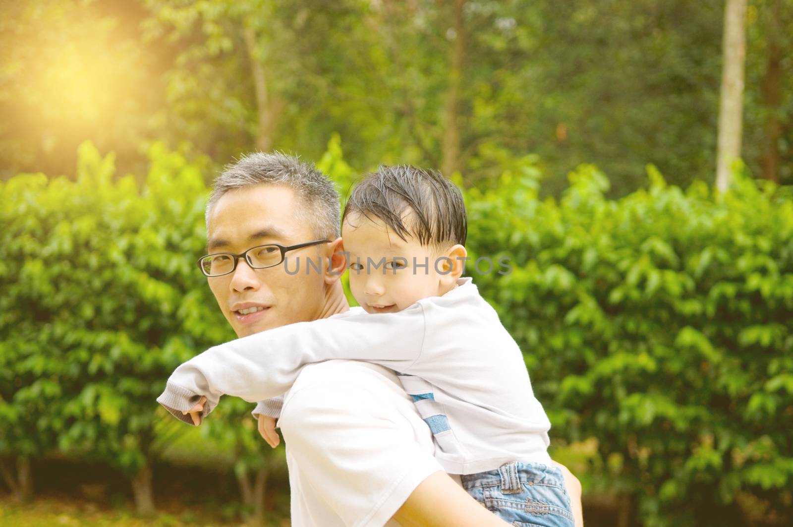 Asian father giving piggyback ride to his son in the evening sunshine