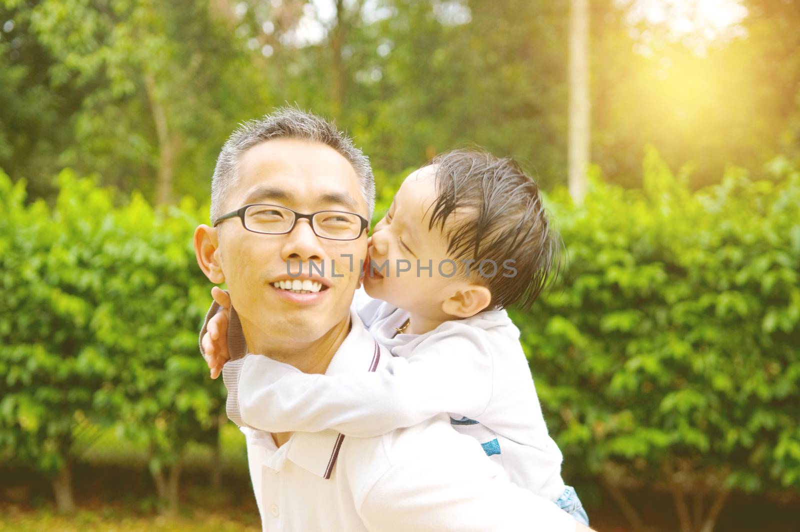 Asian father giving piggyback ride to his son in the evening sunshine