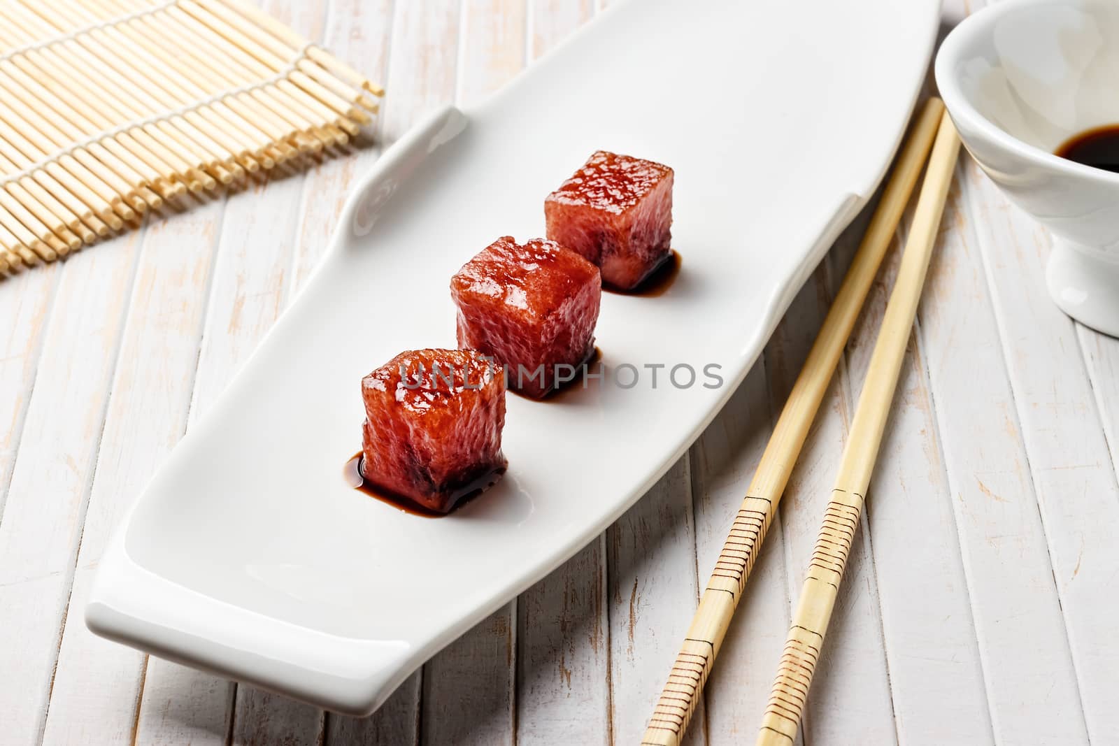 Tuna sashimi dipped in soy sauce with chopsticks and bamboo mat. Raw fish in traditional Japanese style. Horizontal image.