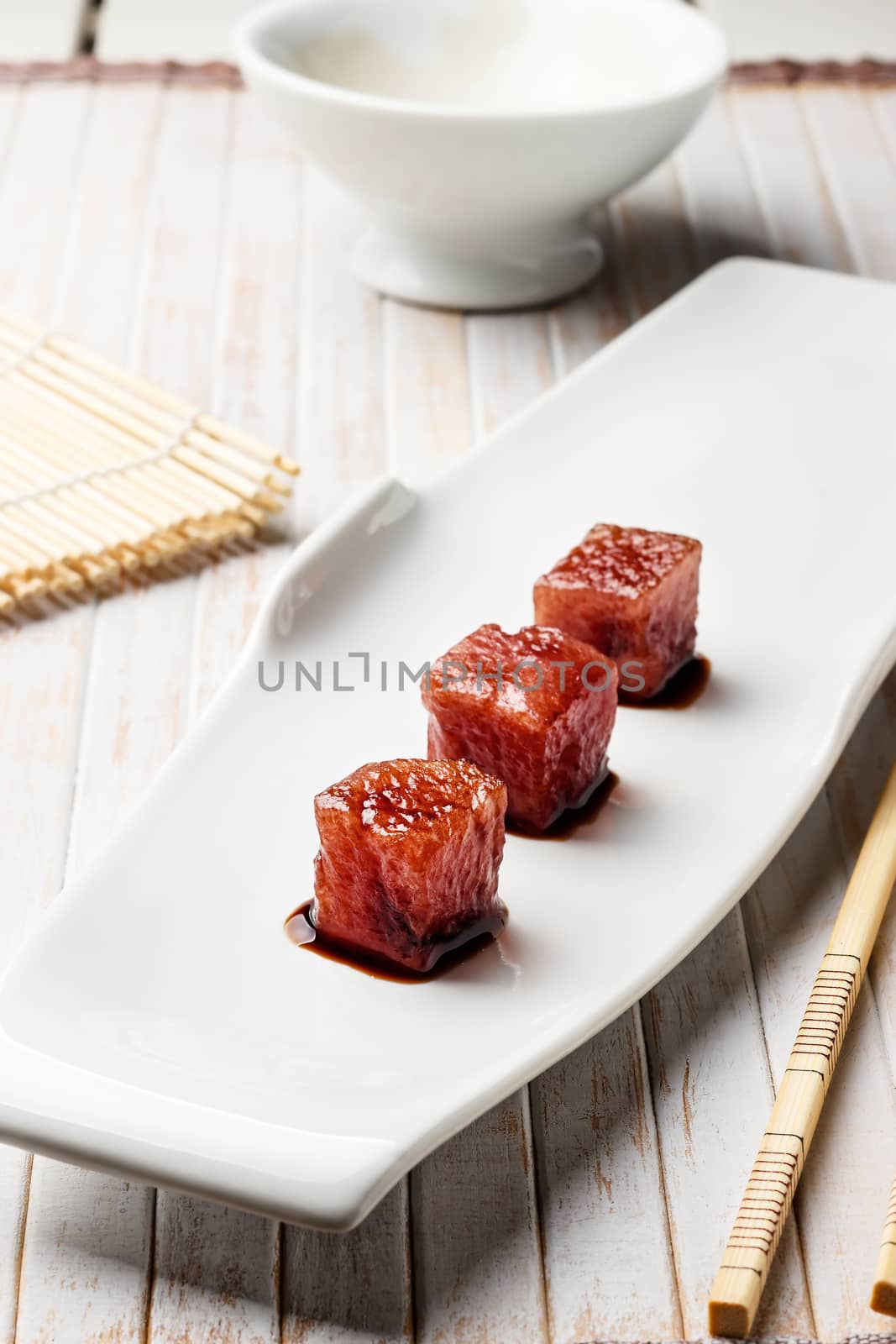 Tuna sashimi dipped in soy sauce with chopsticks and bamboo mat. Raw fish in traditional Japanese style. Vertical image.