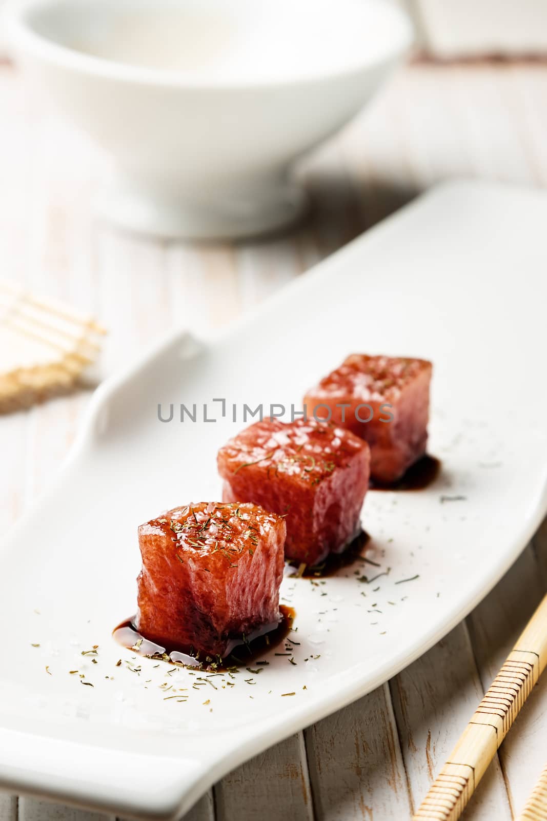Tuna sashimi dipped in soy sauce,  thick salt and dill with chopsticks and bamboo mat. Raw fish in traditional Japanese style. Vertical image.