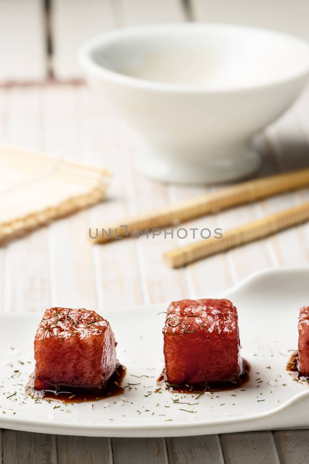 Tuna sashimi dipped in soy sauce,  thick salt and dill with chopsticks and bamboo mat. Raw fish in traditional Japanese style. Vertical image.