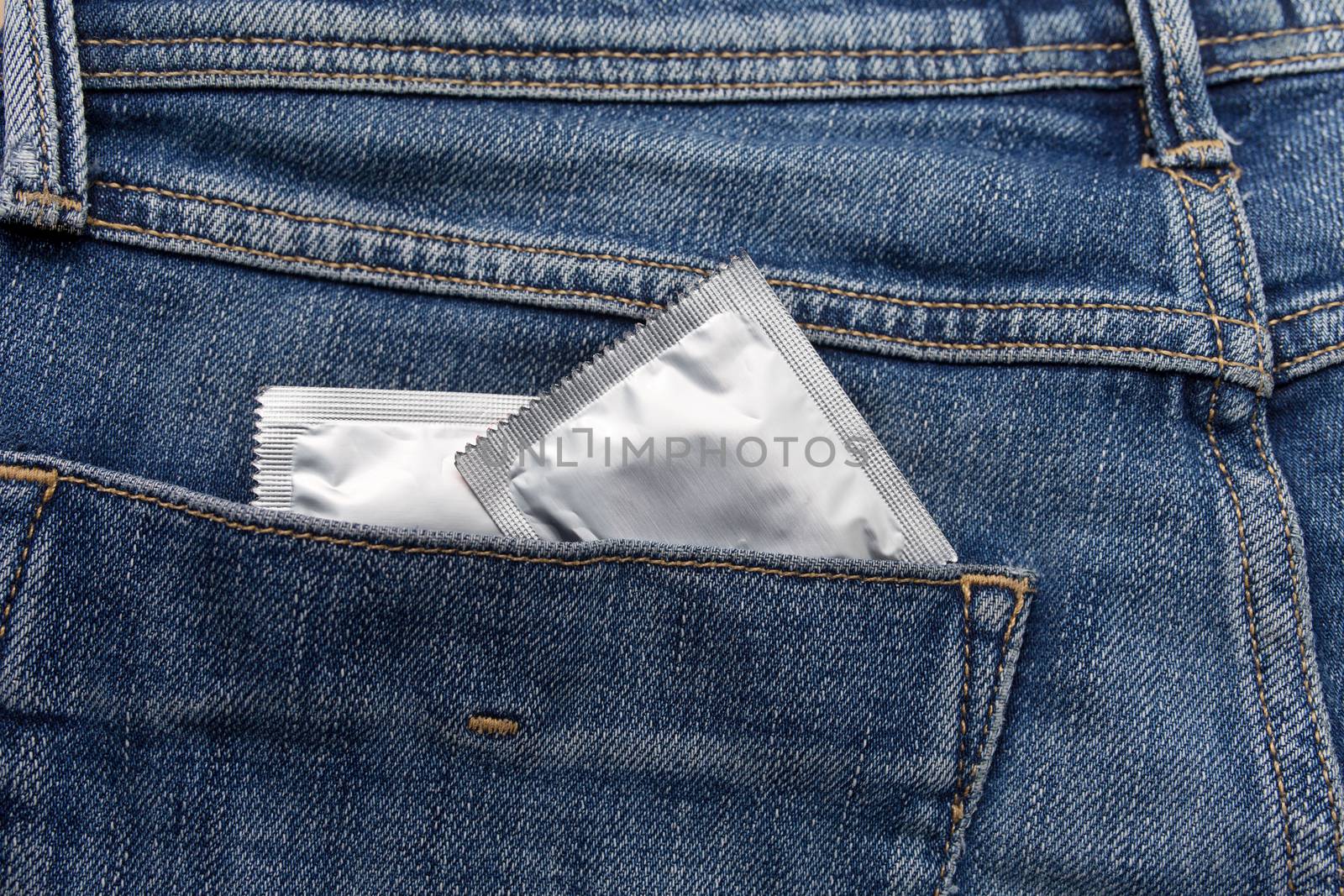 Condom silver color in the pocket of a blue jeans close up