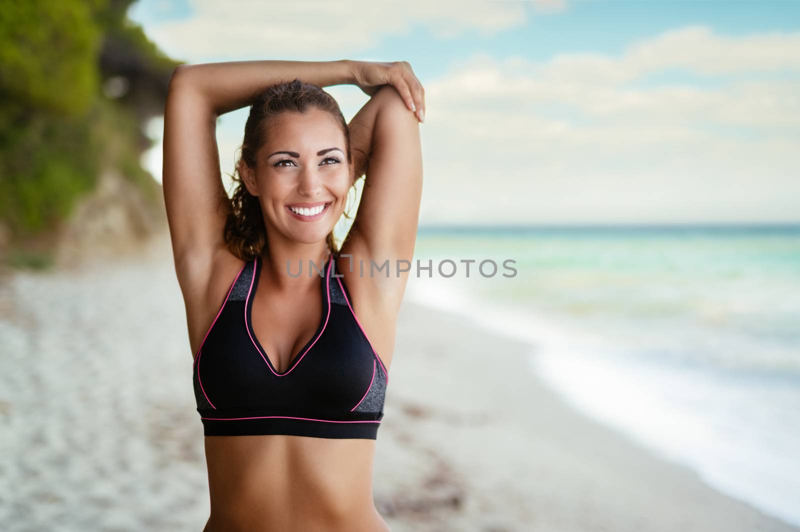 Beautiful young woman doing stretching exercise on the sandy beach.