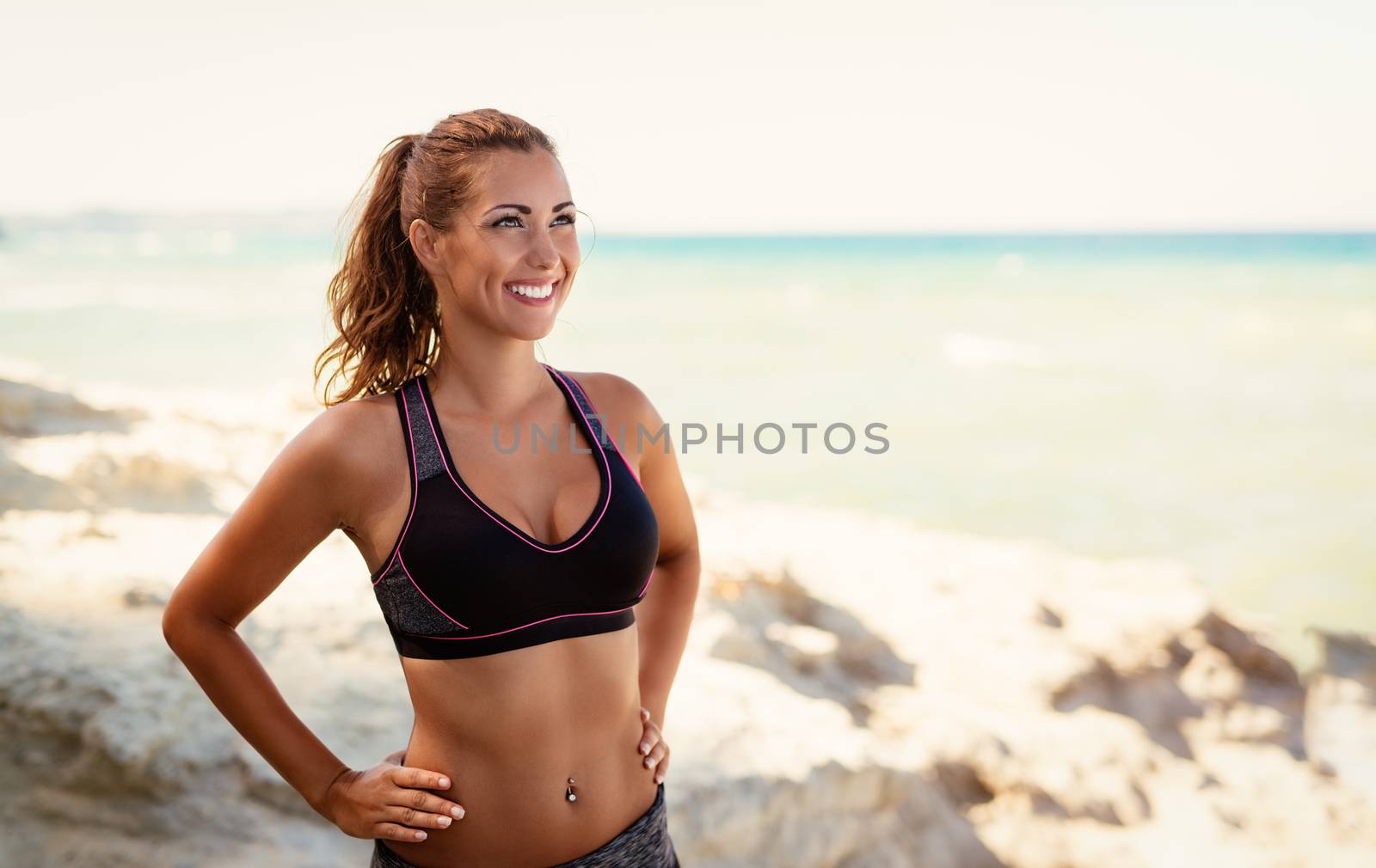 Beautiful young woman relaxing after training on the beach and looking away.