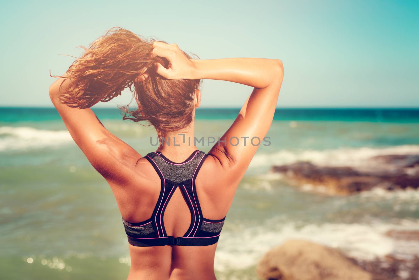 Beautiful young woman relaxing after trainingby the sea. Rear view.