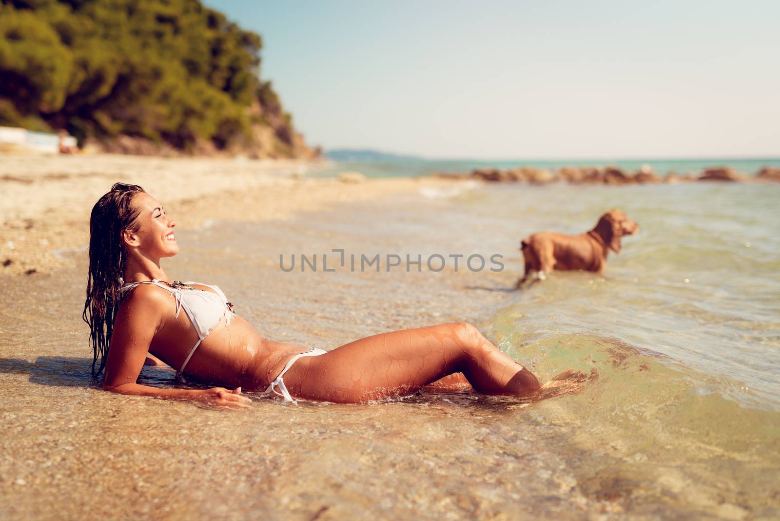 Beautiful young woman enjoying on the beach. She is lounging and sunbathing on the sandy coast in the sea. 
