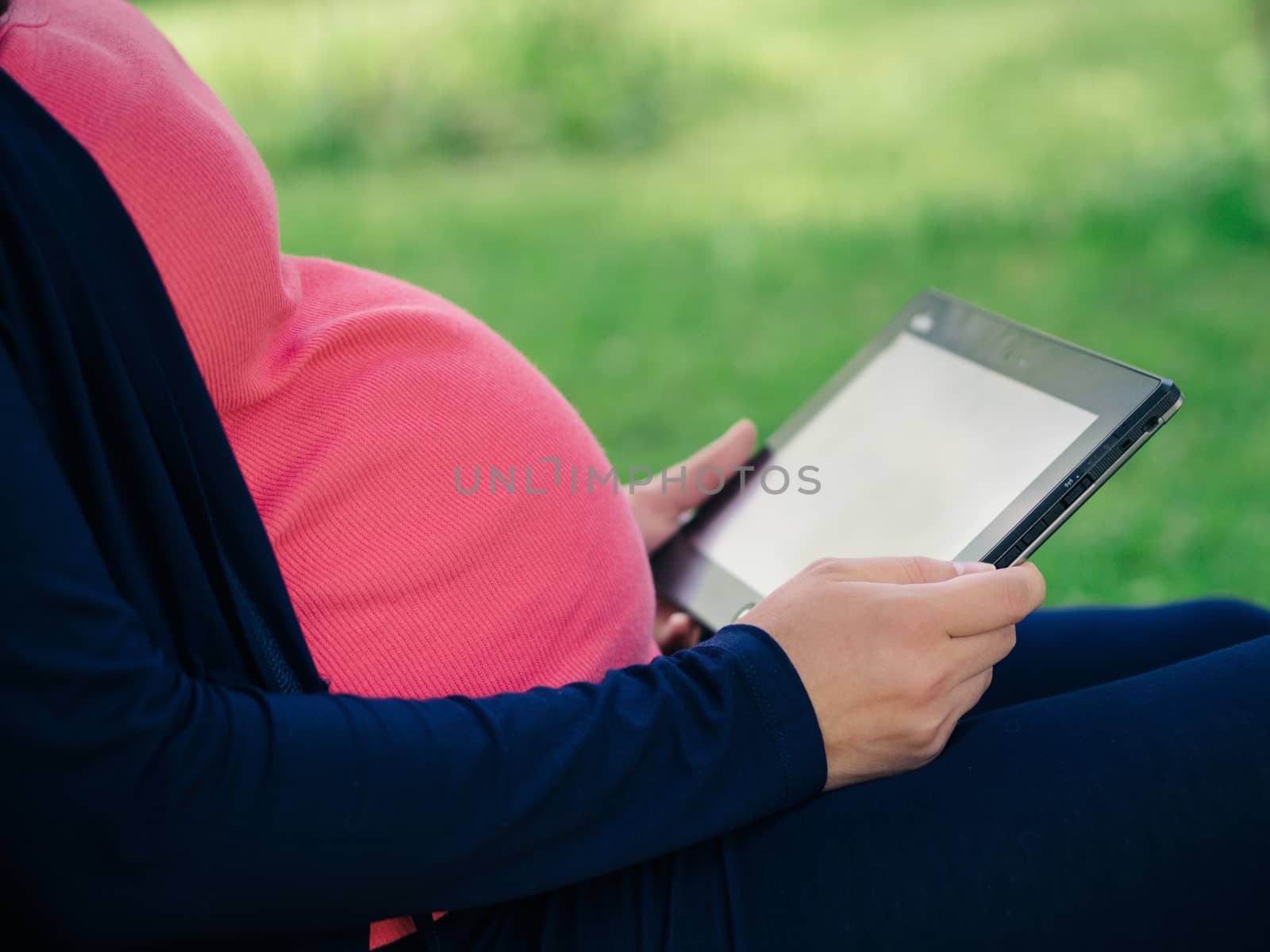 Close up view of pregnant belly and tablet or e-reader. Pregnancy relaxing outdoors concept. Copy space.